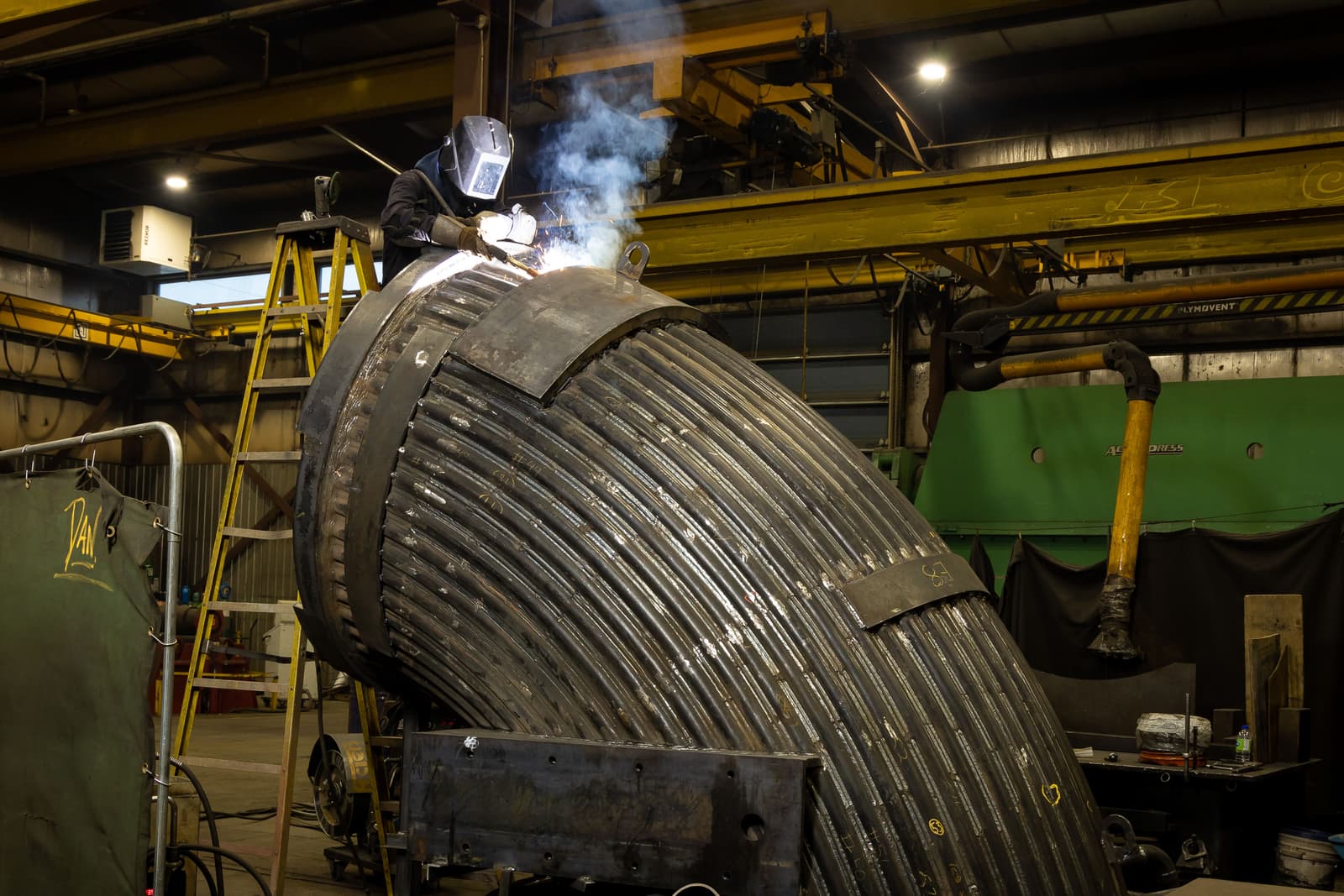 Soudeur en train de souder une grande pièce d'envergure dans l'usine