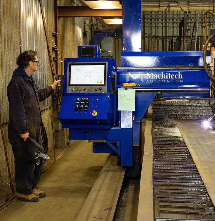 Employé devant une table de coupe avec 1 tête au plasma haute définition 400 AMP,  5 axes. 2 têtes à l'oxycoupage jusqu'à 6'' d'épaisseur"